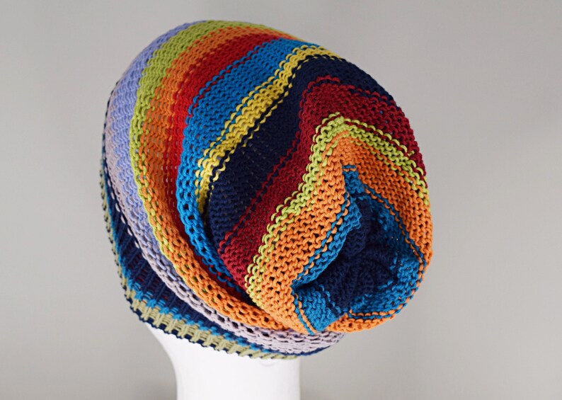 May include: A slouchy knit beanie featuring horizontal stripes in vibrant colors including navy blue, bright orange, red, turquoise, lime green, and light lavender. The hat is constructed with a textured garter stitch pattern throughout.