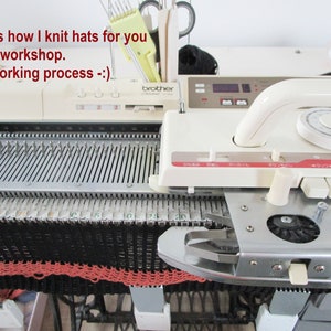 May include: A close-up of a Brother knitting machine in a workshop. The machine is cream-colored with a metal bed, currently knitting a black and coral hat. Text on the machine reads "This is how I knit hats for you in my workshop. The working process -:)".