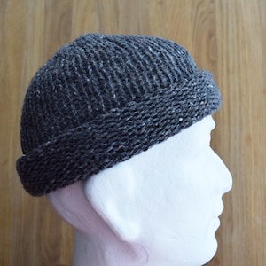 May include: A dark gray knit beanie with a folded brim. The hat is made of a textured yarn with flecks of white. The beanie is displayed on a white mannequin head against a wooden background. This hat is a winter accessory.