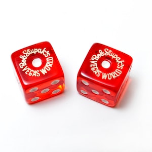 May include: Two red dice with white dots and the text "Bob Stupak's Vegas World" in gold lettering around the top of each die.