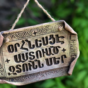 May include: A rustic wooden sign with a brown rope hanging from the top. The sign has a decorative border and the text "or ღ ეს არ არის ღ ძალიან ცუდი" in the Georgian language.
