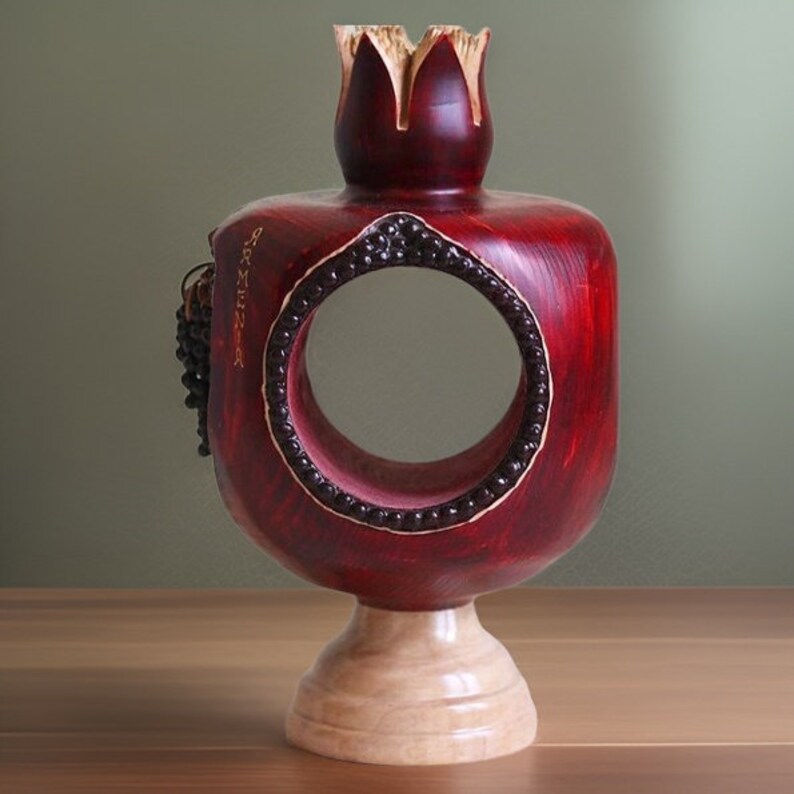 May include: A red wooden pomegranate sculpture with a circular opening and a small wooden base. The pomegranate is carved with details and has a gold inscription.