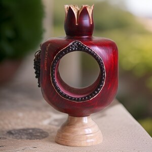 May include: A wooden pomegranate sculpture with a circular opening, painted red with black accents. The sculpture is inscribed with the word "Armenia" and sits on a wooden base.