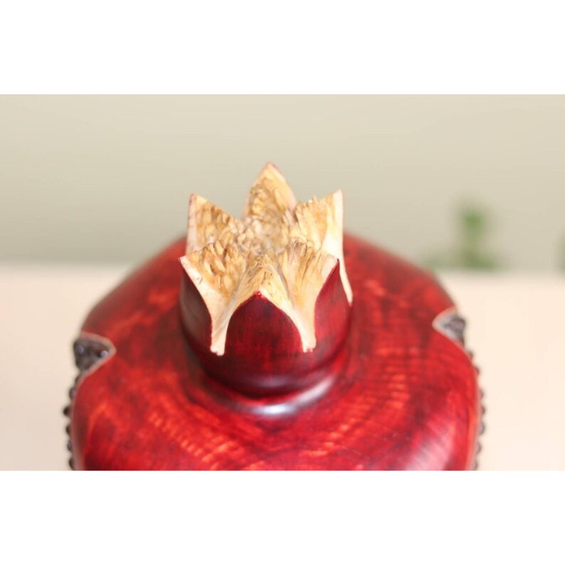 May include: A red wooden pomegranate shaped box with a carved wooden top. The top is a light brown color and has a starburst design.