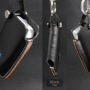 May include: Two leather key fobs with a tan stitching detail. One fob is black and the other is tan. Both fobs have a metal ring and a metal clasp.