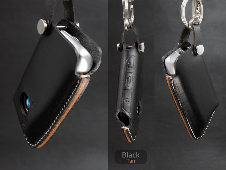 May include: Two leather key fobs with a tan stitching detail. One fob is black and the other is tan. Both fobs have a metal ring and a metal clasp.