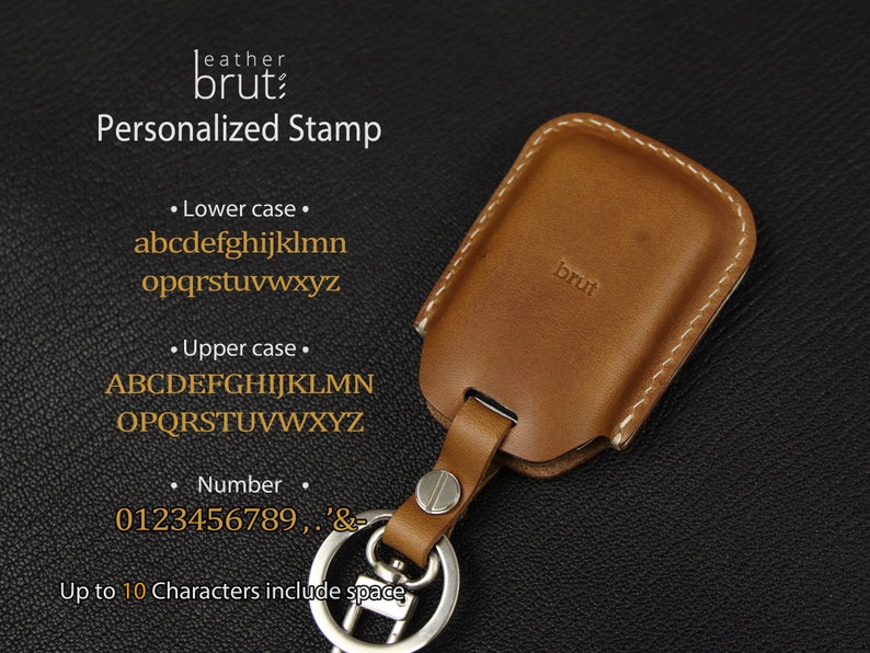 Może przedstawiać: Brązowy sk&oacute;rzany brelok do kluczy ze srebrnym k&oacute;łkiem. Brelok ma białe przeszycia i wygrawerowane słowo "brut" z przodu. Tekst "Personalized Stamp" jest wyświetlany nad brelokiem, wraz z dostępnymi znakami do personalizacji.