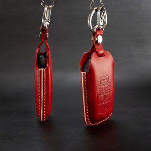 Può includere: Due portachiavi in ​​pelle rossa con anelli argentati. Un portachiavi ha un design cucito e l'altro ha un design cucito con le parole "Hold", "AC", "Rear" e "P" su di esso.