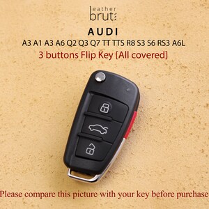 Pu&ograve; includere: Chiave per auto Audi nera con tre pulsanti. La chiave ha un anello in metallo argentato e un accento rosso. Il testo sulla chiave dice "Audi" e "3 buttons Flip Key [All covered]".