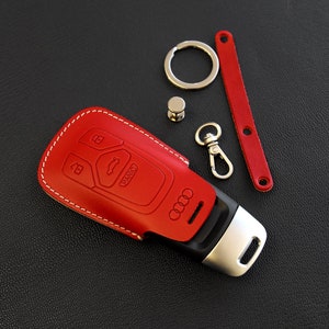 May include: Red leather key fob with white stitching and an Audi logo. The fob has four buttons, including a panic button.