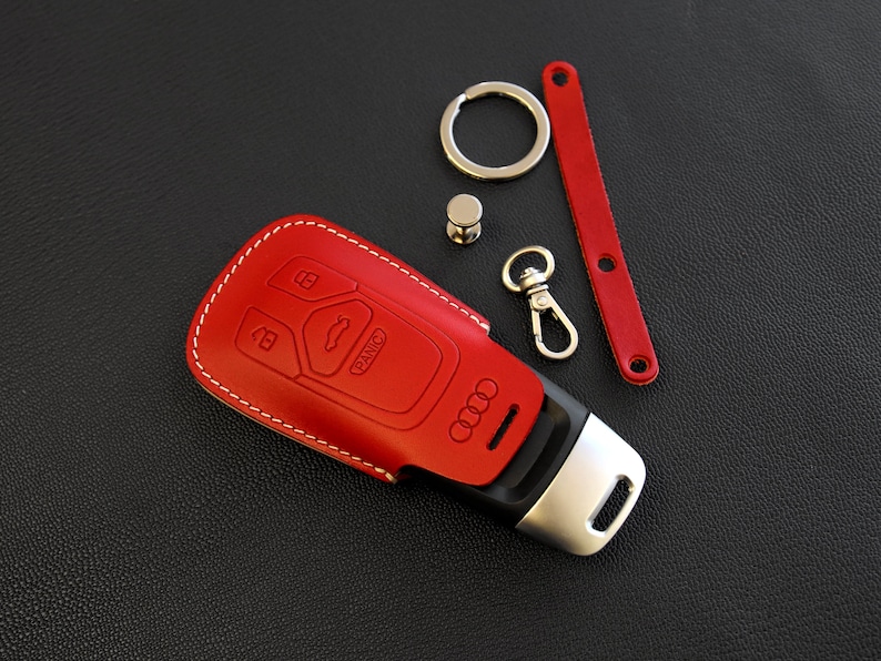 May include: Red leather key fob with white stitching and an Audi logo. The fob has four buttons, including a panic button.