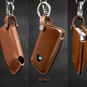 May include: A brown leather key fob with a silver key ring and a stitched edge. The fob has a cutout for a car key and a logo on the front.