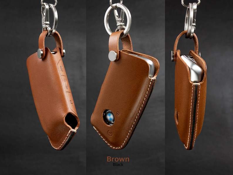May include: A brown leather key fob with a silver key ring and a stitched edge. The fob has a cutout for a car key and a logo on the front.