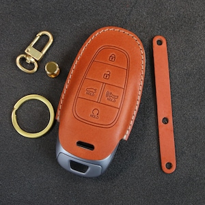May include: A brown leather key fob with stitching around the edges. The fob has a silver key with buttons labeled "Hold".