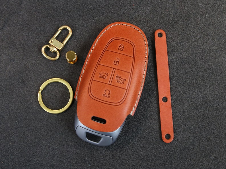 May include: A brown leather key fob with stitching around the edges. The fob has a silver key with buttons labeled "Hold".