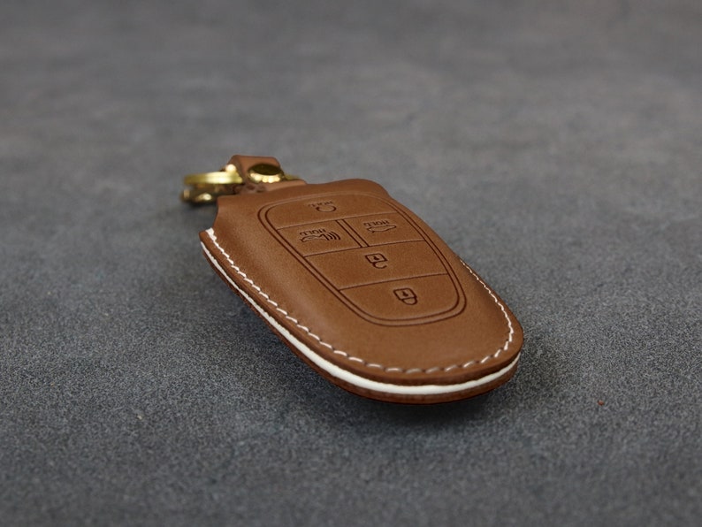 May include: A brown leather key fob with white stitching. The fob has four buttons with symbols for lock, unlock, trunk, and panic.