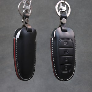 May include: Two black leather key covers with red stitching and silver key rings. One key cover has a silver button and the other has three buttons.