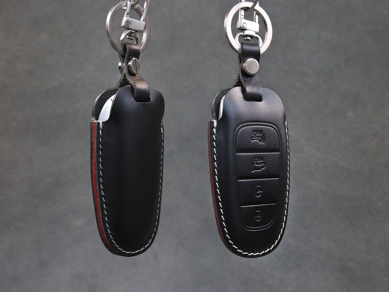 May include: Two black leather key covers with red stitching and silver key rings. One key cover has a silver button and the other has three buttons.