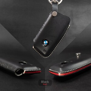 May include: Black leather key fob cover with a white stitching detail. The cover has a red accent on the bottom edge.