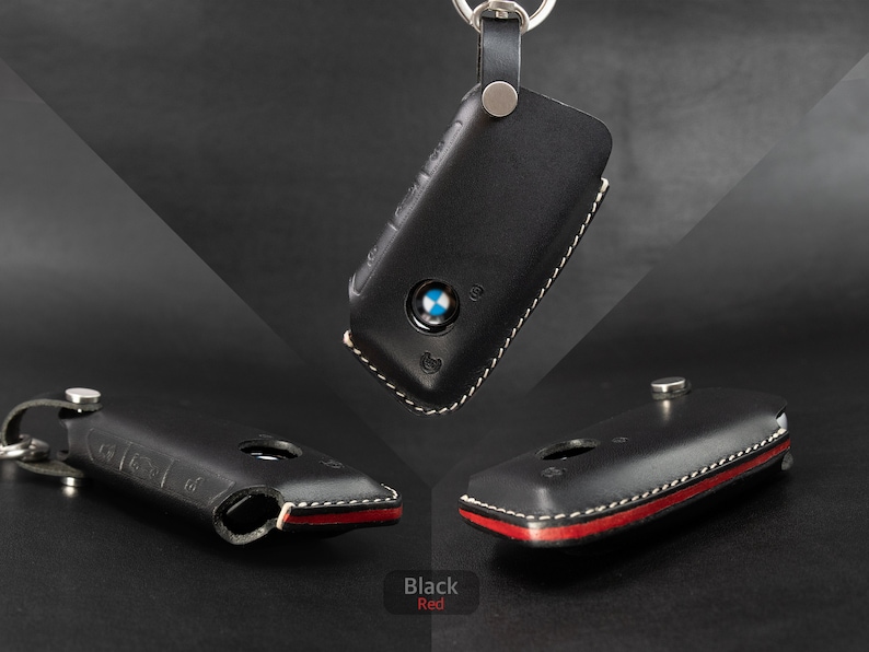 May include: Black leather key fob cover with a white stitching detail. The cover has a red accent on the bottom edge.