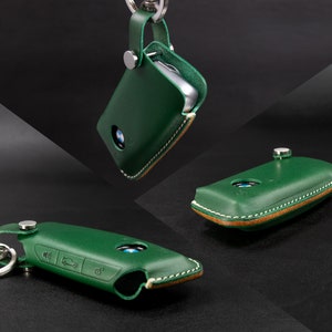 May include: Green leather key fob with tan stitching and a silver key ring. The fob has a BMW logo and buttons for locking, unlocking, and trunk release.
