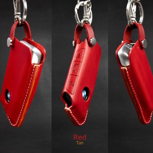 May include: Red leather key fob with a tan stitching detail. The fob has a silver metal loop and a silver metal snap closure.