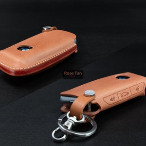 May include: Two leather key fobs in rose tan color. One fob is closed and the other is open with a silver key ring attached. The open fob has a car icon and a lock icon embossed on it.