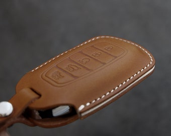 May include: A brown leather key fob with white stitching. The fob has four buttons with symbols for unlock, lock, trunk, and panic.