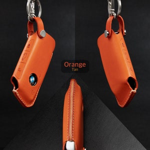 May include: Orange leather key fob with a silver key ring and a BMW logo. The key fob has a stitched seam and a button on the side.