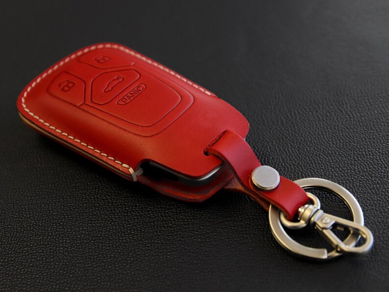 May include: Red leather key fob with a silver key ring and a key chain. The fob has a stitched edge and the text "PANIC" is visible on the key fob.