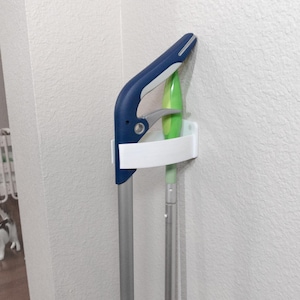 May include: A white plastic wall-mounted mop and broom holder with a blue and silver mop handle and a green mop head.