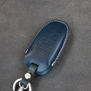 May include: A blue leather key fob with white stitching and a key ring. The fob has multiple buttons with symbols for car functions.
