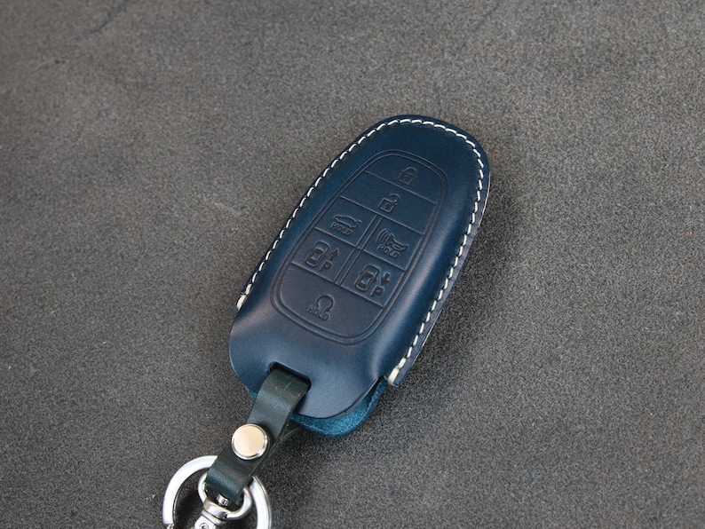 May include: A blue leather key fob with white stitching and a key ring. The fob has multiple buttons with symbols for car functions.