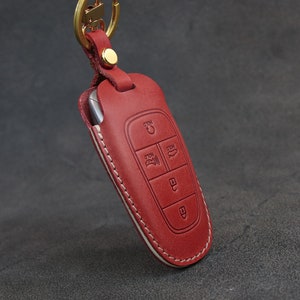 May include: Red leather key fob with a white stitching detail. The fob has a key chain loop and multiple buttons.