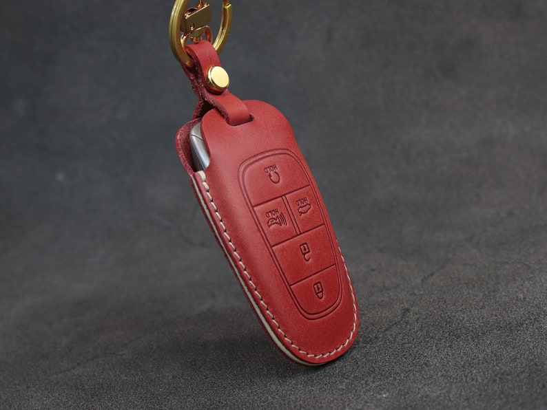 May include: Red leather key fob with a white stitching detail. The fob has a key chain loop and multiple buttons.