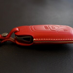 May include: Red leather key fob with a white stitching detail. The fob has a key chain attached.