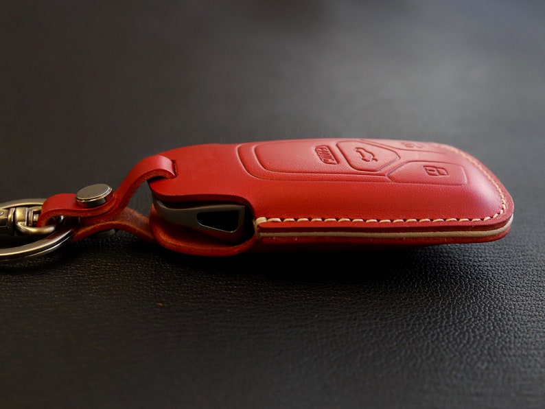 May include: Red leather key fob with a white stitching detail. The fob has a key chain attached.
