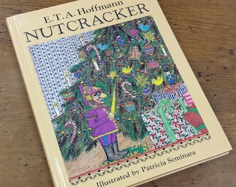 May include: A book titled "E.T.A. Hoffmann NUTCRACKER" with illustrations of a Christmas tree, presents, and a nutcracker soldier. The book is illustrated by Patricia Seminara.