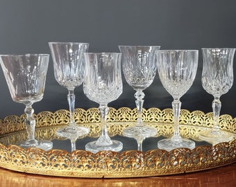 May include: Six clear glass wine glasses with a diamond pattern on a gold mirrored tray with a decorative edge.