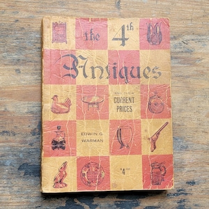 May include: The 4th Antiques and Their Current Prices book cover features a checkered pattern with illustrations of various antiques, including a rooster, a table, a bottle, a gun, a pitcher, and a goblet. The book cover is yellowed and worn, giving it a vintage look.
