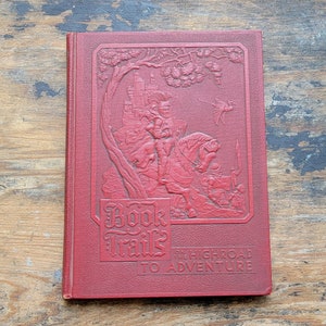 May include: A red hardback book with the title "Book Trails on the Highroad to Adventure". The cover features an embossed illustration of a knight riding a horse through a forest.