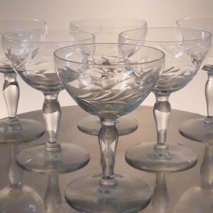 May include: Set of six clear glass stemmed drinking glasses with an etched floral design. The glasses have a wide bowl and a delicate stem.