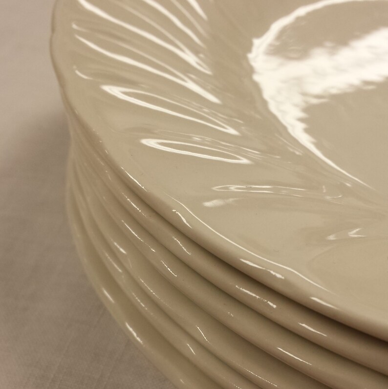Peut inclure: Une pile d'assiettes en c&eacute;ramique blanc cass&eacute;. Chaque assiette pr&eacute;sente un motif de bordure cannel&eacute; et tourbillonnant. Les assiettes sont empil&eacute;es, la premi&egrave;re &eacute;tant mise au point.