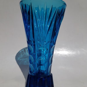 May include: A blue glass vase with a textured, geometric design. The vase has a wide mouth and a narrow base.