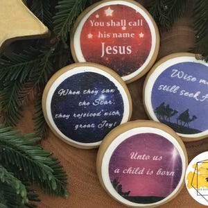 Può includere: Quattro biscotti natalizi rotondi decorati con immagini e testo. I biscotti presentano un biscotto rosso e bianco con il testo "You shall call his name Jesus", un biscotto blu e bianco con il testo "When they saw the Star, they rejoiced with great Joy!", un biscotto viola e bianco con il testo "Unto us a child is born", e un biscotto blu e bianco con il testo "Wise men still seek Him".