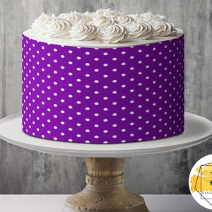 Könnte beinhalten: Lilafarbener Kuchen mit weißem Frosting und weißen Punkten. Der Kuchen steht auf einem weißen Kuchenständer mit Holzsockel.