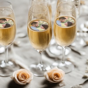 May include: Champagne flutes filled with sparkling wine, each featuring a circular image of a couple. Soft peach roses and a neutral-toned tablecloth complete the celebratory scene, perfect for a wedding or anniversary.