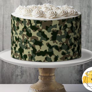 May include: A white cake with green, brown, and tan camouflage frosting. The cake is on a white cake stand with a wooden base.
