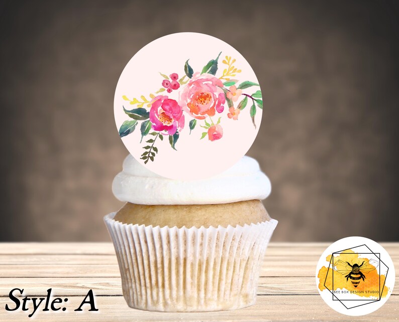 K&ouml;nnte beinhalten: Ein Cupcake mit einem runden, wei&szlig;en Frosting-Oberteil und einem essbaren Topper mit pinkfarbenem und gelbem Blumendesign. Der Cupcake steht auf einer Holzoberfl&auml;che. Der essbare Topper tr&auml;gt den Text "Style: A".
