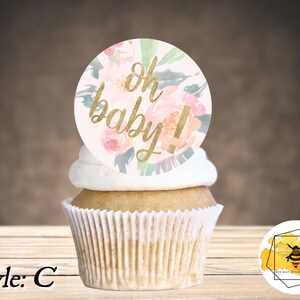 K&ouml;nnte beinhalten: Ein Cupcake, der mit einem runden, rosa und goldenen, floralen Cupcake-Topper verziert ist, auf dem "oh baby!" steht.